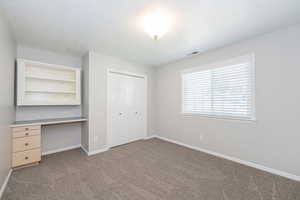 Unfurnished bedroom featuring light colored carpet, a textured ceiling, a desk, and a closet