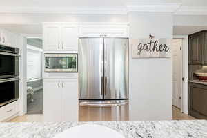 Kitchen featuring appliances with stainless steel finishes, ornamental molding, light wood-style flooring, light stone countertops, and white cabinets