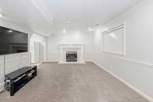 Unfurnished living room with a tiled fireplace, a textured ceiling, light colored carpet, and ornamental molding