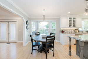 Eat in kitchen space featuring light wood-style floors, recessed lighting, french doors, ornamental molding, and arched walkways
