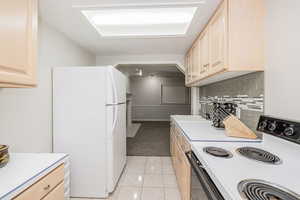 Kitchen with white appliances, light brown cabinets, light countertops, light tile patterned floors, and decorative backsplash