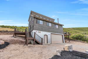 Rear view of house with a deck, stairs, an attached garage, and dirt driveway
