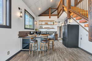 Kitchen with open shelves, refrigerator with ice dispenser, high vaulted ceiling, light wood-style floors, and a breakfast bar area