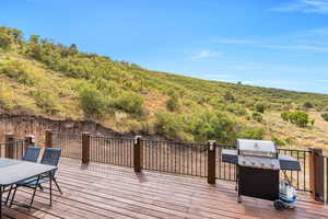 Wooden terrace featuring a grill, a wooded view, and outdoor dining area