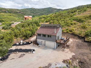 Back of property with an attached garage, a deck with mountain view, dirt driveway, and stairs