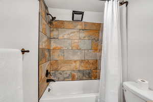 Bathroom featuring shower / bathtub combination with curtain and toilet