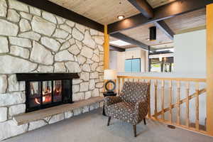 Living area featuring carpet flooring, a wood ceiling with exposed beams, and a fireplace