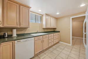 Kitchen featuring light brown cabinets, white appliances, dark countertops, light tile patterned floors, and recessed lighting