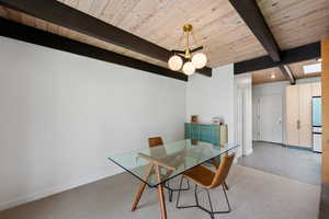 Carpeted dining area with baseboards and a wood ceiling with exposed beams