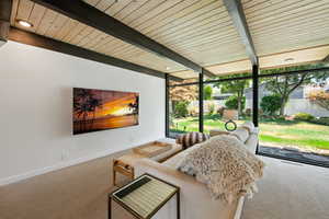 Sunroom / solarium featuring expansive windows, carpet, and a wood ceiling with exposed beams
