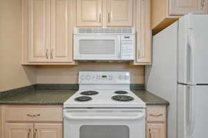 Kitchen with white appliances, light brown cabinets, and dark countertops