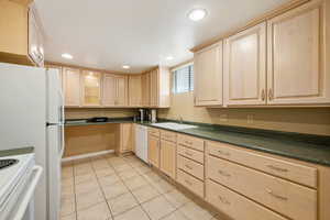 Kitchen featuring light brown cabinetry, dark countertops, light tile patterned floors, recessed lighting, and white appliances