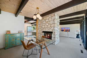Dining area featuring a stone fireplace, carpet, and a wooden ceiling with exposed beams