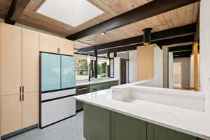 Kitchen featuring white refrigerator, green cabinets, a skylight, light stone countertops, and light brown cabinetry
