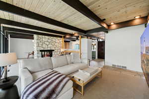 Carpeted living area with a stone fireplace, a wood ceiling with exposed beams, and recessed lighting