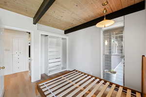 Unfurnished bedroom with a closet, light wood-style floors, and a wooden ceiling with exposed beams