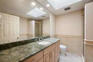 Full bath with vanity, a skylight, tile walls, a shower stall, and light tile patterned floors