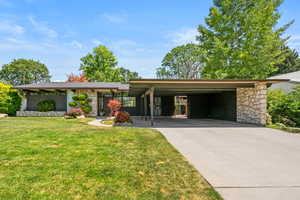View of front facade with stone siding, a front lawn, and driveway