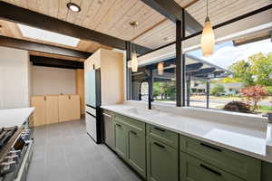 Kitchen featuring green cabinets, appliances with stainless steel finishes, beamed ceiling, dark tile patterned flooring, and a skylight