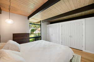 Bedroom with multiple closets, floor to ceiling windows, light wood finished floors, and beam ceiling