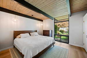 Bedroom featuring expansive windows, light wood finished floors, and a wooden ceiling with exposed beams