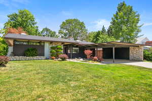 Mid-century modern home featuring stone siding, driveway, a front lawn, an attached carport, and a chimney