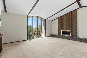 Unfurnished living room featuring a brick fireplace, carpet, and a wall of windows