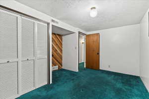 Unfurnished bedroom featuring dark carpet, a textured ceiling, a closet, and wooden walls