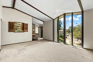 Carpeted spare room with beamed ceiling, a wall of windows, and high vaulted ceiling