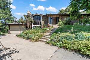 Mid-century inspired home with brick siding, driveway, a chimney, a sunroom, and a front lawn
