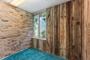 Unfurnished room with carpet flooring, brick wall, and a textured ceiling
