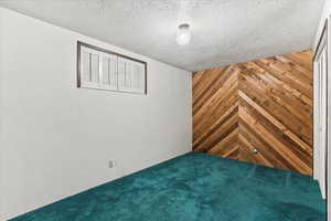Unfurnished bedroom with wooden walls, a closet, a textured ceiling, and carpet floors