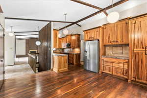 Kitchen with brown cabinets, decorative light fixtures, stainless steel appliances, decorative backsplash, and dark wood-type flooring
