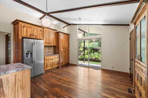 Kitchen with brown cabinets, stainless steel refrigerator with ice dispenser, dark wood-style floors, decorative backsplash, and decorative light fixtures