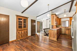 Kitchen with brown cabinets, pendant lighting, light countertops, freestanding refrigerator, and dark wood-type flooring
