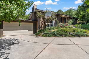 View of front of home with driveway, brick siding, a garage, and a chimney
