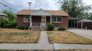 Bungalow-style home featuring covered porch, a carport, driveway, a chimney, and brick siding