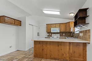 Kitchen with a peninsula, brown cabinets, light countertops, open shelves, and lofted ceiling