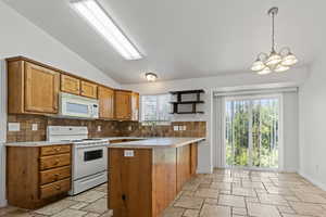 Kitchen featuring a peninsula, decorative backsplash, lofted ceiling, light countertops, and white appliances