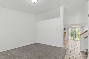Spare room with stairs, a chandelier, vaulted ceiling, stone tile flooring, and carpet