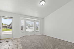 Foyer with a textured ceiling, stone tile flooring, vaulted ceiling, and light colored carpet