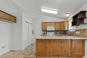 Kitchen with a peninsula, light countertops, brown cabinets, vaulted ceiling, and open shelves