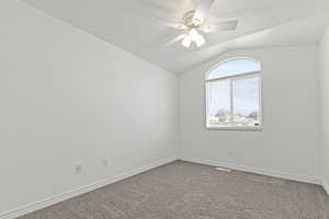 Empty room with vaulted ceiling, carpet, ceiling fan, and a textured ceiling