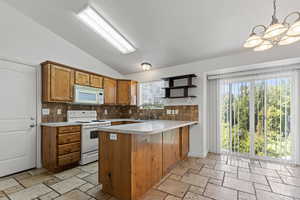 Kitchen with lofted ceiling, open shelves, brown cabinetry, white appliances, and a peninsula