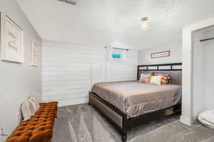 Carpeted bedroom featuring a textured ceiling and wooden walls