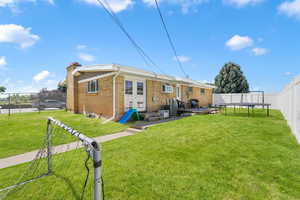 Rear view of property with a fenced backyard, a trampoline, brick siding, and a chimney