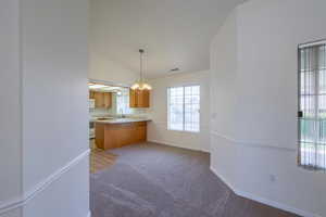 Kitchen with light countertops, light carpet, decorative light fixtures, lofted ceiling, and a peninsula