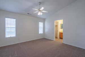 Unfurnished bedroom featuring lofted ceiling, dark carpet, ceiling fan, and ensuite bath