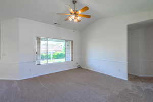 Carpeted spare room featuring vaulted ceiling and ceiling fan
