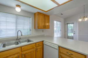 Kitchen featuring dishwasher, light countertops, pendant lighting, brown cabinets, and a chandelier